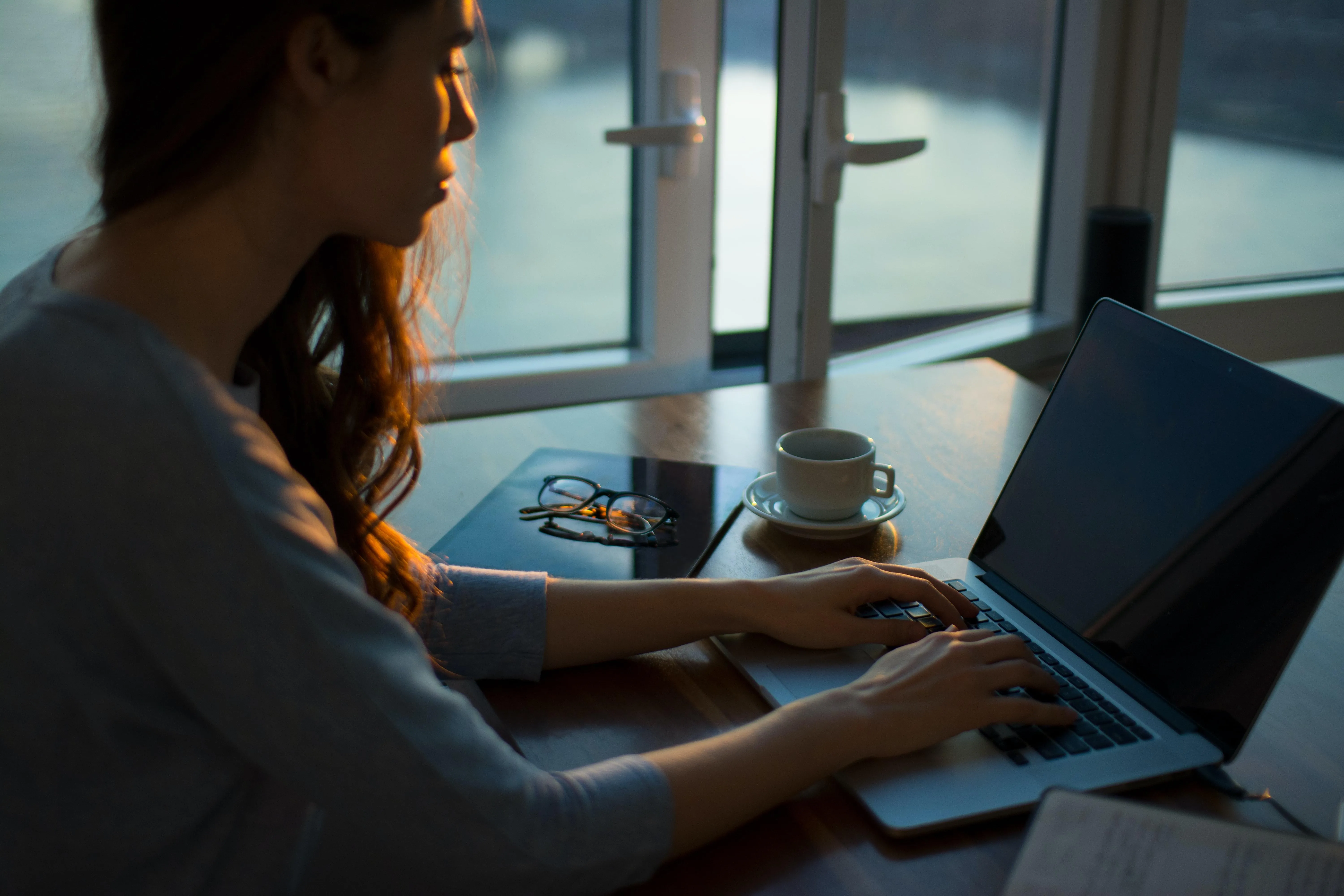 side view of a woman with long brown hair typing on a laptop computer